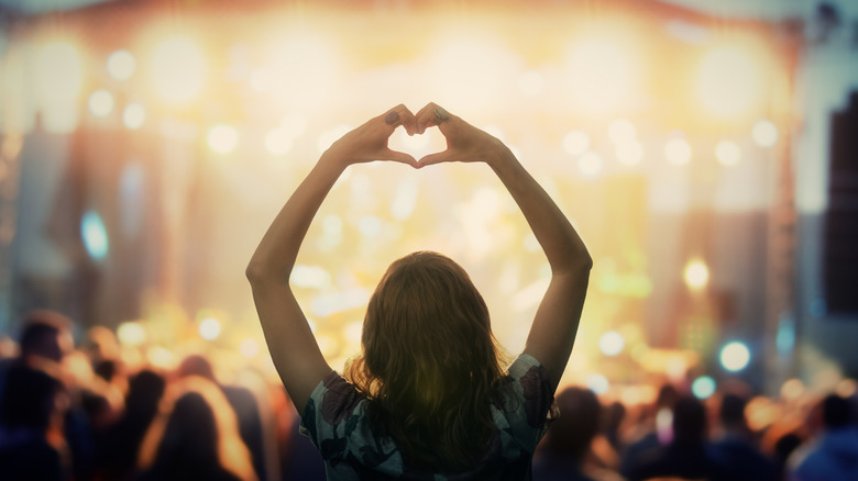 Mujer formando un corazón con las manos en un concierto