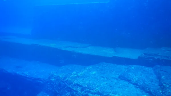 Buzo explorando las terrazas de arenisca del Monumento Yonaguni bajo el agua cristalina frente a la isla de Yonaguni, Japón