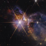 Imagen en infrarrojo del telescopio James Webb del sistema FS Tau, con protoestrellas FS Tau A y FS Tau B y chorros de material sobrecalentado en naranja y rojo sobre un fondo de galaxias distorsionadas por el polvo
