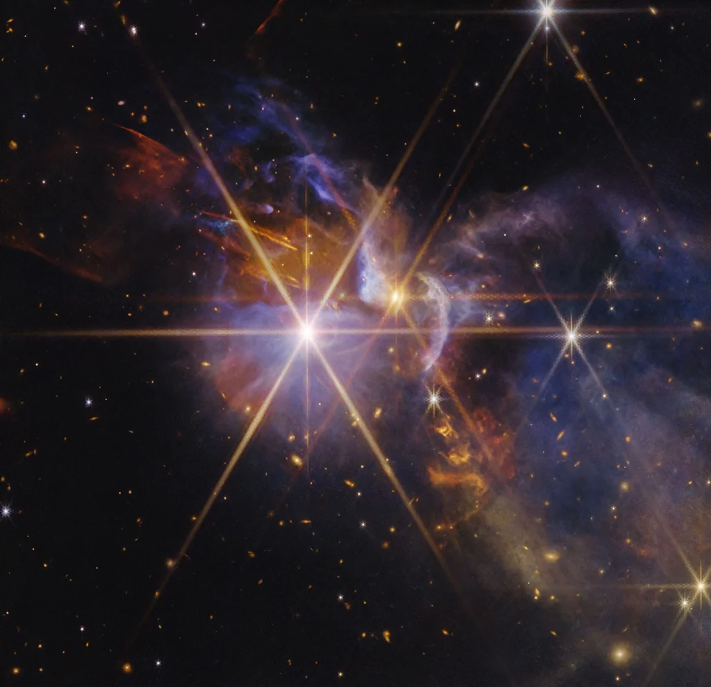 Imagen en infrarrojo del telescopio James Webb del sistema FS Tau, con protoestrellas FS Tau A y FS Tau B y chorros de material sobrecalentado en naranja y rojo sobre un fondo de galaxias distorsionadas por el polvo